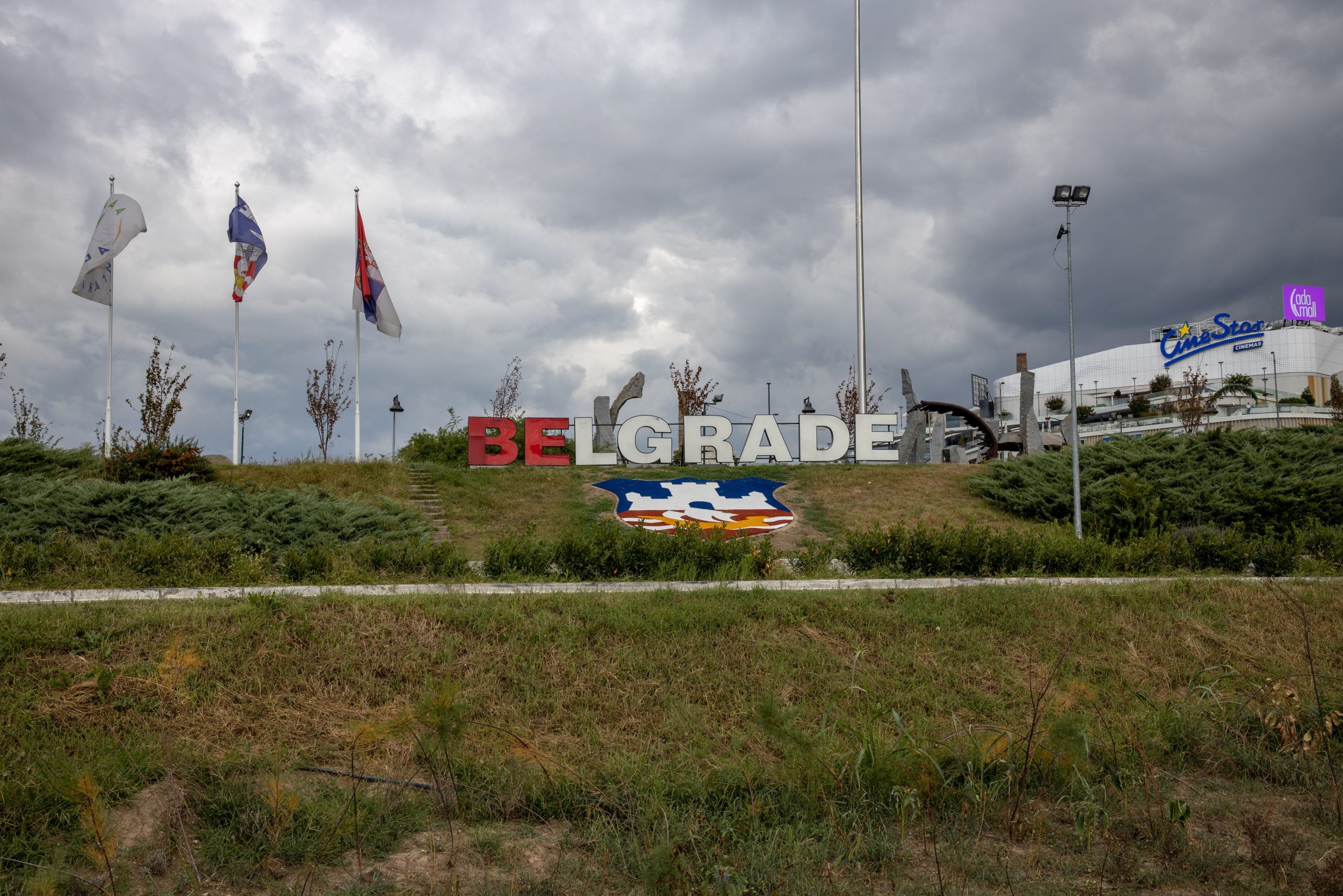 Large Belgrade sign in a park setting with flags on a cloudy day, Serbia