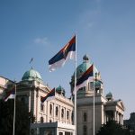 Serbian parliament building with national flags on a clear day.