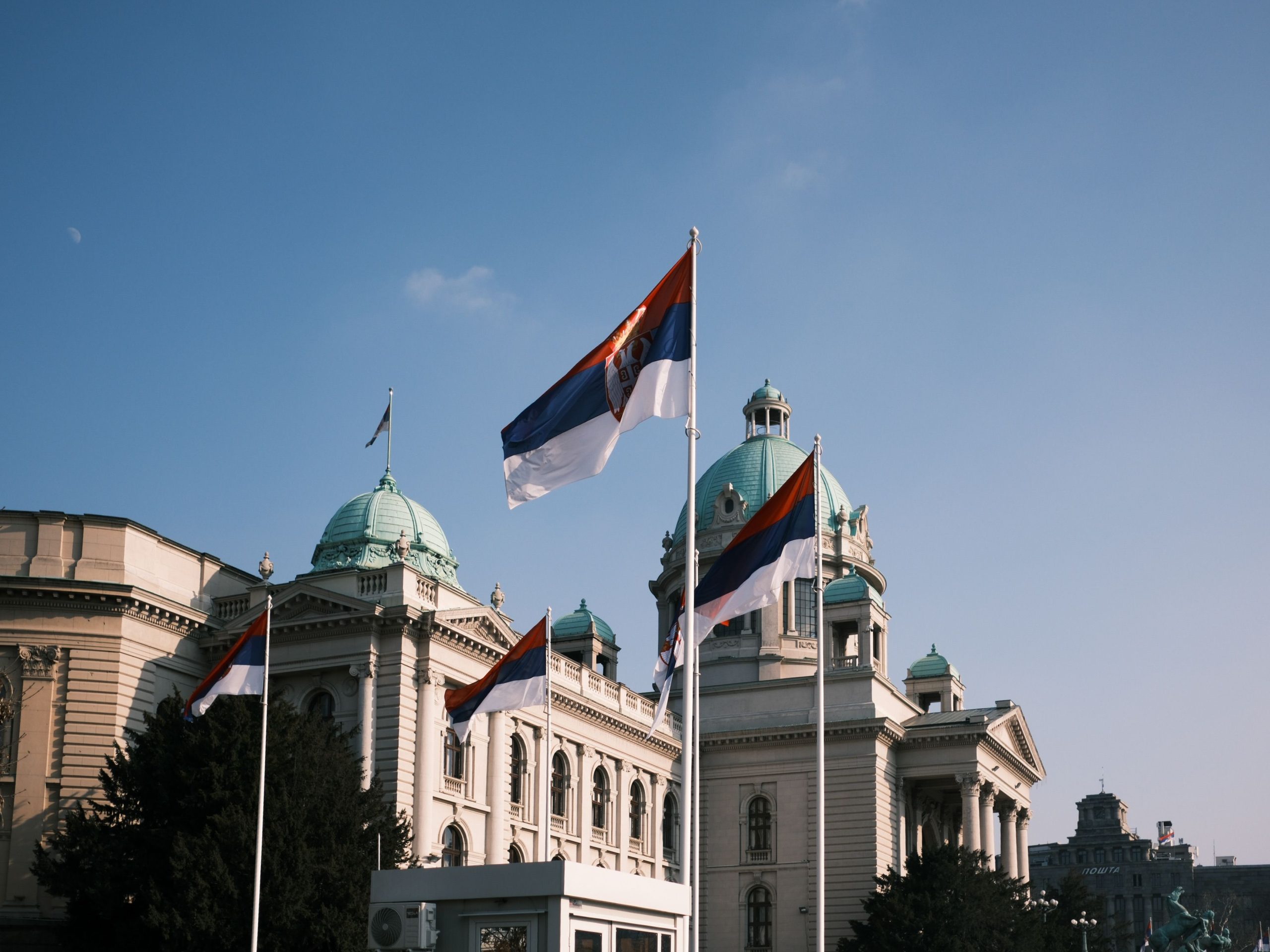 Serbian parliament building with national flags on a clear day.