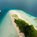 Discover the serene beauty of Jolly Buoy Island's white sandy beach and turquoise waters from above.
