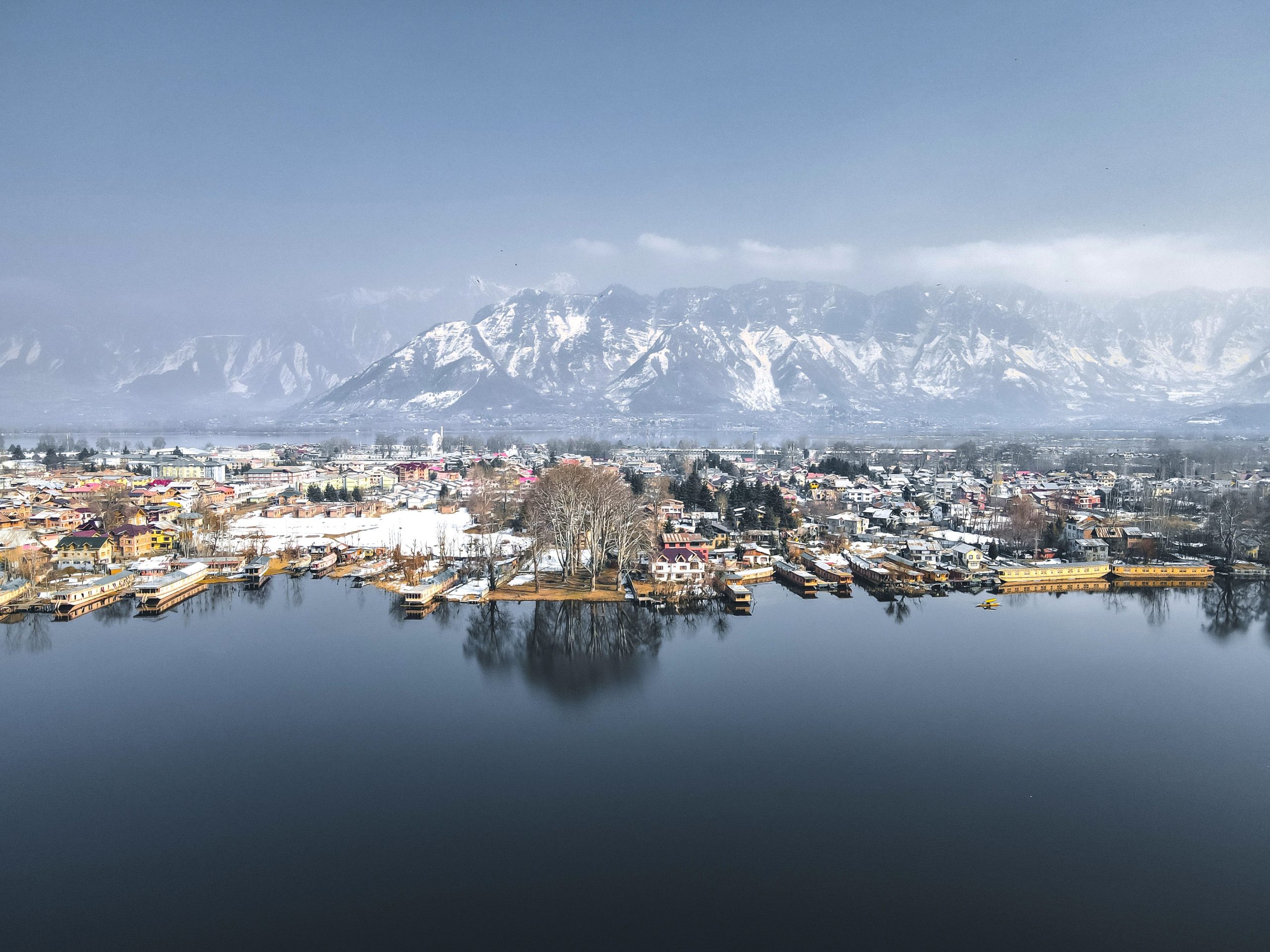 Scenic aerial view of Srinagar city with the Himalayas in the background, reflecting in tranquil waters.